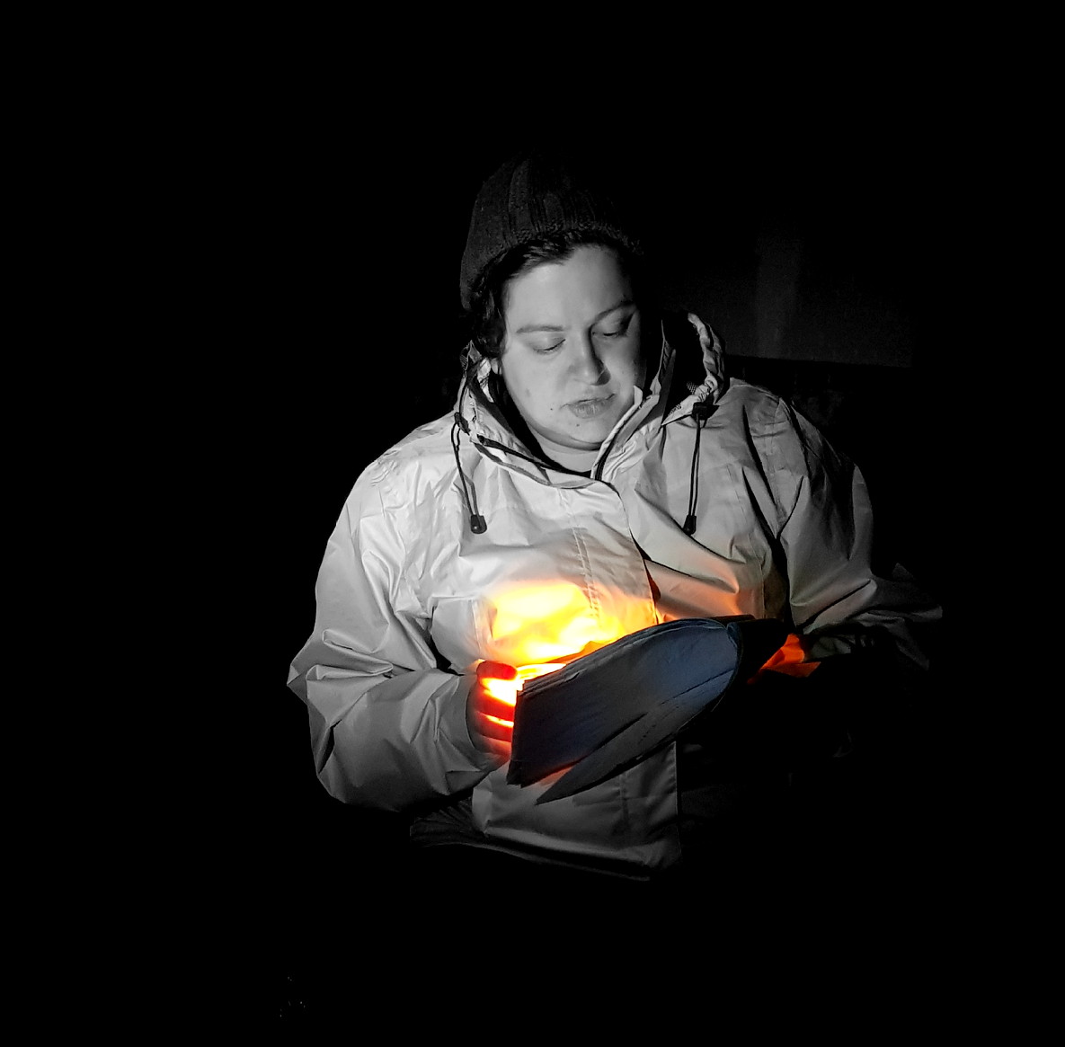 A woman sitting in the dark reading a poem by candle light