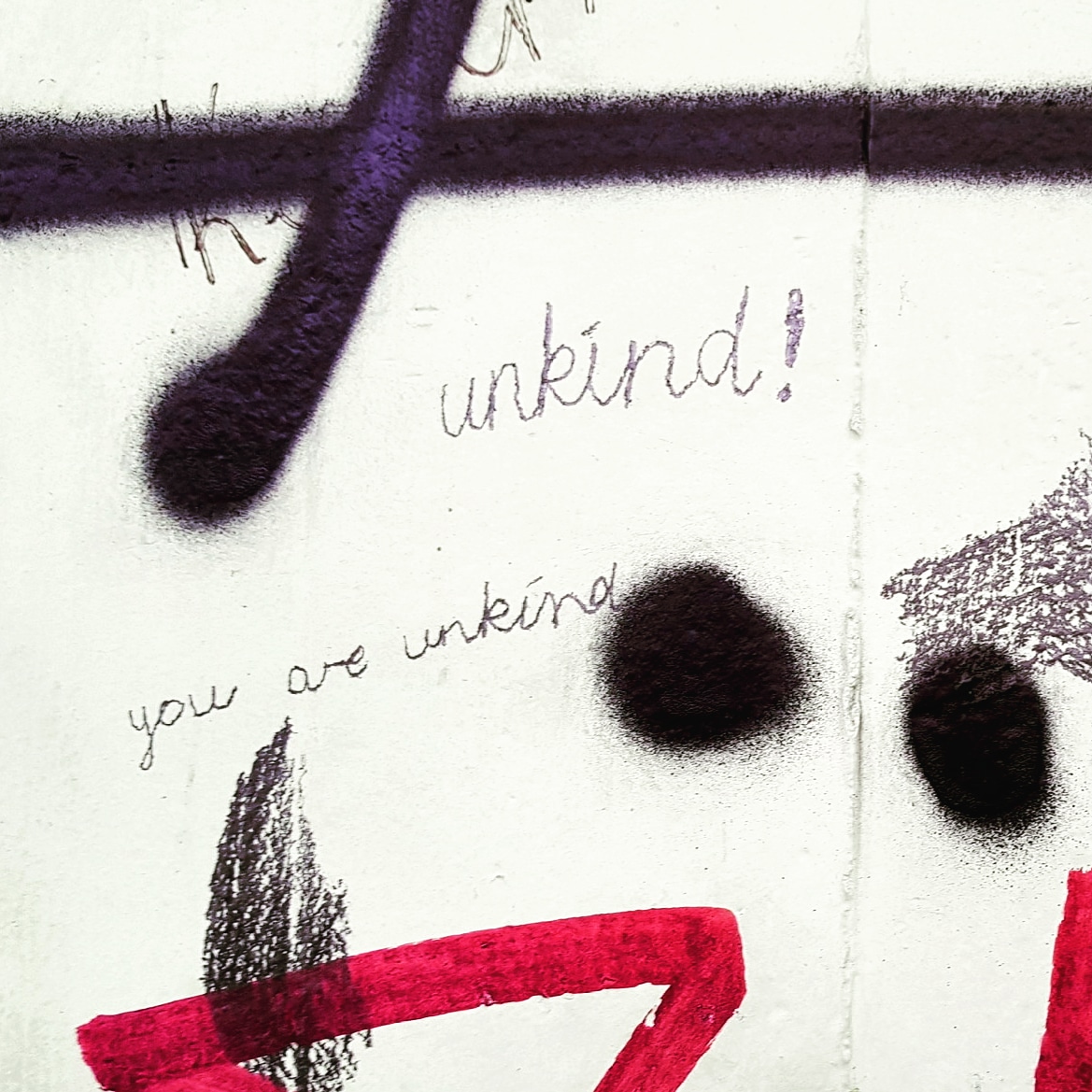 red and black graffiti on a wall including the words 'unkind' and 'you are unkind'