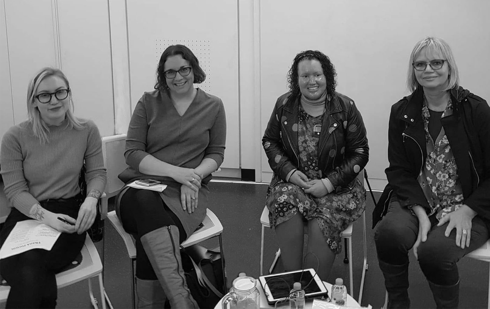 Black and white photo of four women sitting on chairs facing the camera. Women from right to left are: Gaele Sobott, Carly Findlay, Kate Larsen and Jessica Alice. 